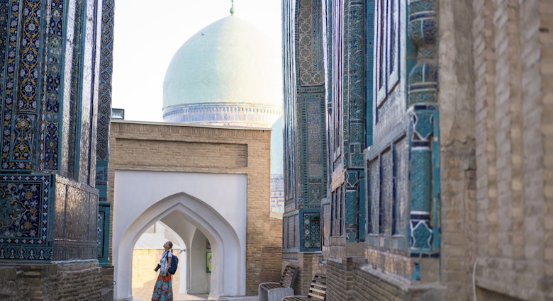 Senior woman on the path between memorial buildings of Shakhi Zinda  Mausoleum which is memorial complex of Islamic architecture from 9 to 12. century in Samarkand, Uzbekistan
1129859652
ancient, architecture, art, asia, building exterior, craft, cultures, decoration, east, entrance, facade, famous place, history, indigenous culture, monument, multi colored, old, pattern, photography, religion, sky, spirituality, travel destinations, unesco world heritage site, mausoleum, silk road, tomb, samarkand, tribal art, central asia, mosaic, ceramics, cemetery, memorial, uzbekistan, tile, turquoise colored, persian culture, photography themes, footpath, single lane road, horizontal, women, one woman only, senior adult, shah-i-zinda
A woman looking up at the memorial buildings of Shah-I-Zinda Mausoleums in Samarkand, Uzbekistan