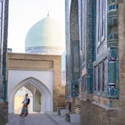 Senior woman on the path between memorial buildings of Shakhi Zinda  Mausoleum which is memorial complex of Islamic architecture from 9 to 12. century in Samarkand, Uzbekistan
1129859652
ancient, architecture, art, asia, building exterior, craft, cultures, decoration, east, entrance, facade, famous place, history, indigenous culture, monument, multi colored, old, pattern, photography, religion, sky, spirituality, travel destinations, unesco world heritage site, mausoleum, silk road, tomb, samarkand, tribal art, central asia, mosaic, ceramics, cemetery, memorial, uzbekistan, tile, turquoise colored, persian culture, photography themes, footpath, single lane road, horizontal, women, one woman only, senior adult, shah-i-zinda
A woman looking up at the memorial buildings of Shah-I-Zinda Mausoleums in Samarkand, Uzbekistan