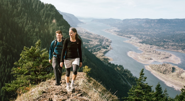 A fit older adult couple in their 50's hike up a rocky trail on a mountain ridge, the beautiful Columbia river gorge spreading out behind them.  They smile as they continue up the ascent.  Horizontal with copy space.
493237716
Trail, Couple - Relationship, Climbing, Outdoor Pursuit, Mature Women, Women, Men, Two People, Beauty In Nature, Columbia River, 50-59 Years, Mature Adult, Backpack, Smiling, Moving Up, Exercising, Columbia River Gorge, Healthy Lifestyle, Majestic, Discovery, Happiness, Exploration, Nature, Lifestyles, Content, Cheerful, Hiking, Gray Hair, People, Oregon, Tree, Mountain Ridge, Mountain, Attractive Person
A woman and man hiking in the hills above Columbia River Gorge