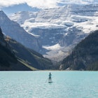 woman paddleboards across mountain lake