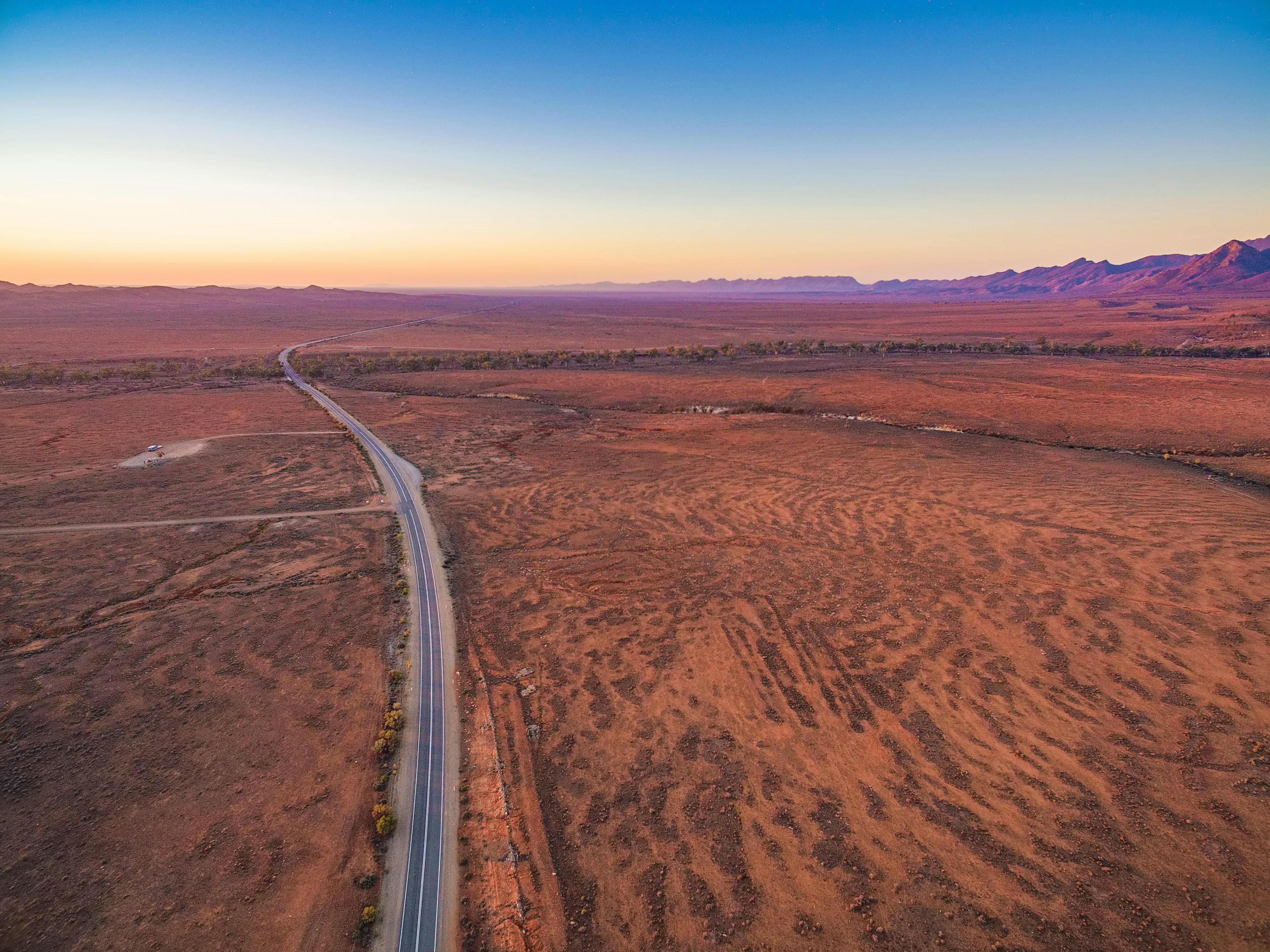 Aerial view of road passing through red desert land at sunset