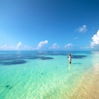 A girl stands in the shallow water of a turquoise ocean