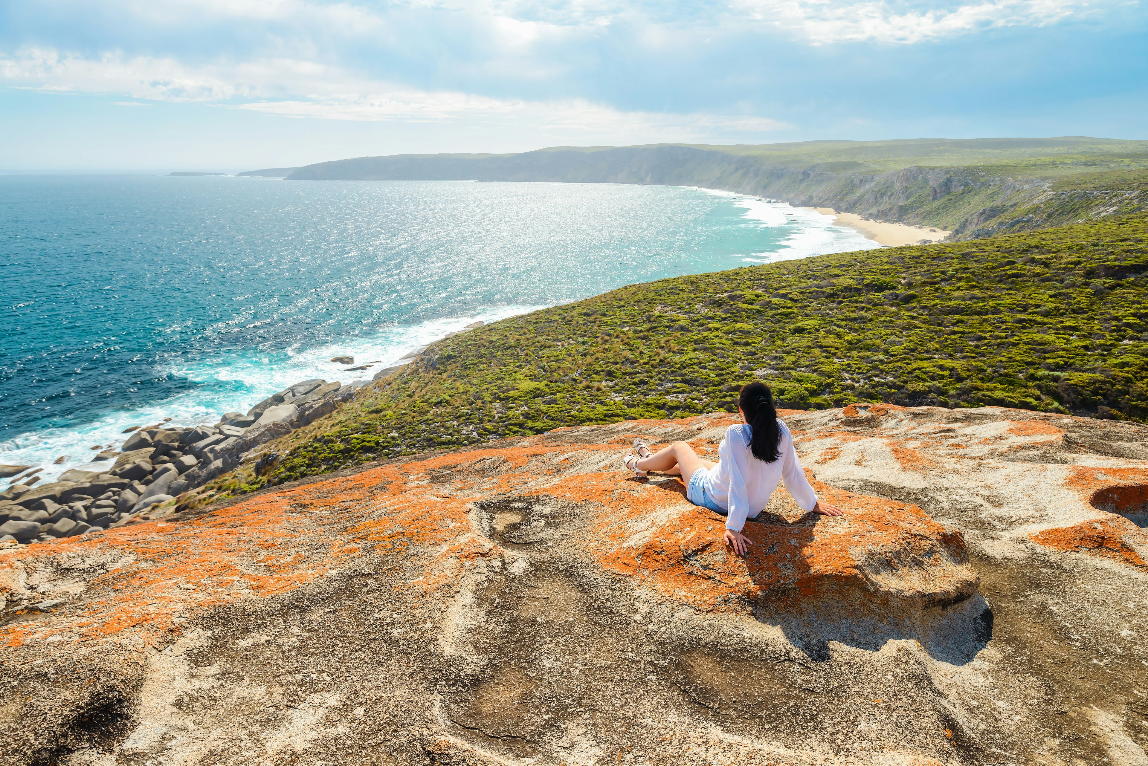A woman sits on a clifftop looking out at the coastal scenery