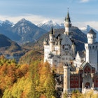 Famous castle Neuschwanstein in fall colours. Autumn. Lake alpsee and the alps with snow in background
