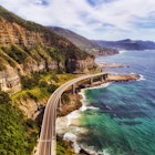 Aerial of the Sea Cliff Bridge near steep sandstone cliffs on the Grand Pacific drive along pacific coast of Australia.
787893667
australia, nsw, sea cliff bridge, wollongong, aerial, bend, blue, bridge, cliff, clifton, coast, destination, driving, edge, grand pacific drive, highway, horizon, infrastructure, landmark, lane, mid-air, modern, mountains, nobody, pacific, ranges, road, sandstone, say, scenic, sea, seascape, steep, summer, sunlight, surf, tide, tourism, traffic, transportation, waterfront, waves